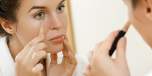 orretivo liquido e creme. Foto mulher branca passando corretivo abaixo dos olhos sobre o espelho