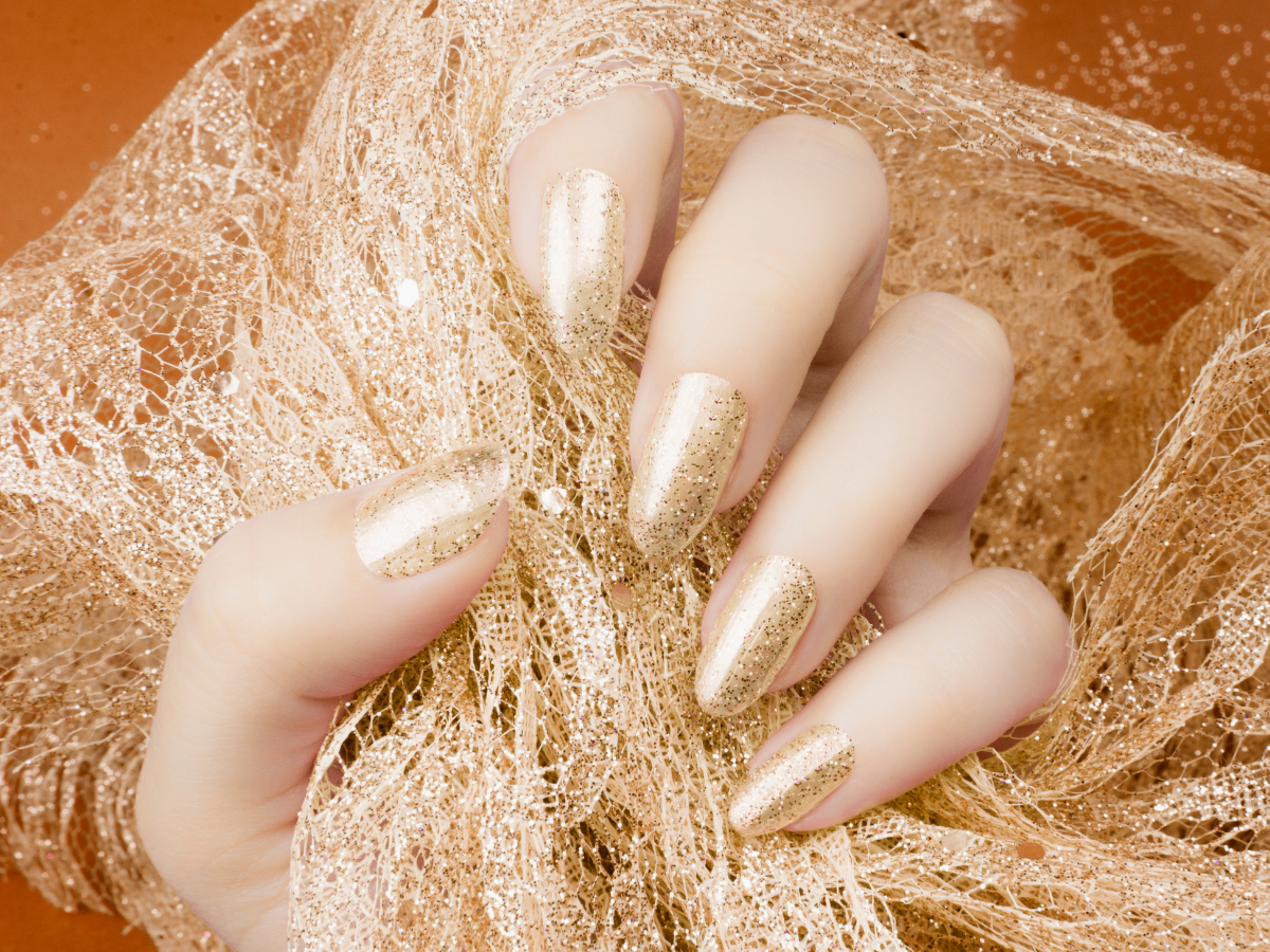 Fairy nails. Foto mão de uma mulher com a unha pintada de nude alaranjado com glitter.