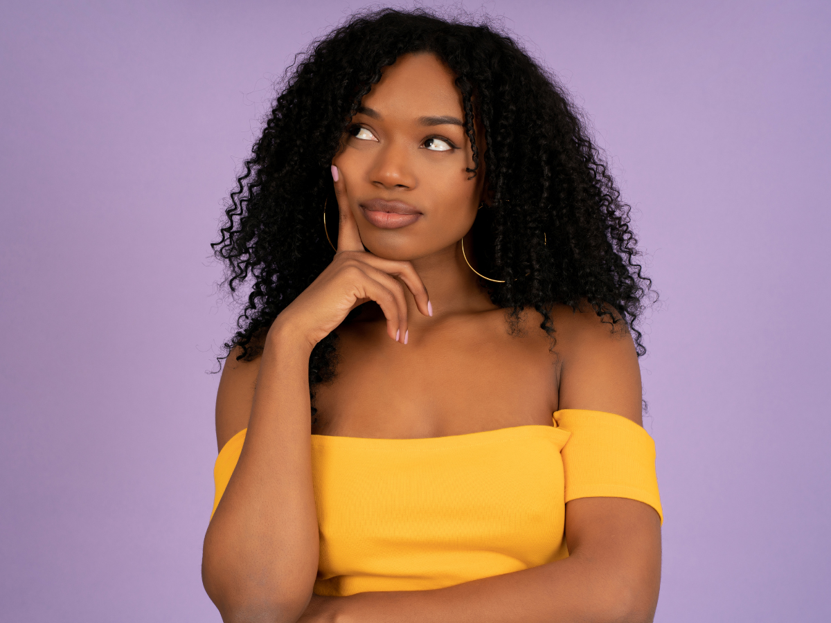 Mitos e verdades sobre cabelos. Foto mulher negra e blusa laranja com cara de dúvida