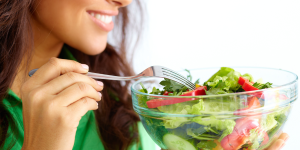 Impacto da alimentação na pele. Foto possui uma mulher branca com camiseta verde e um pote de salada
