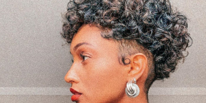 Corte pixie cut para cabelos cacheados. Foto mulher negra com pixie cut nos cachos virada de lateral