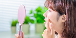 Pele oleosa, produtos essenciais para o skincare. Foto mulher japonesa olhando o espelho e observando a pele.