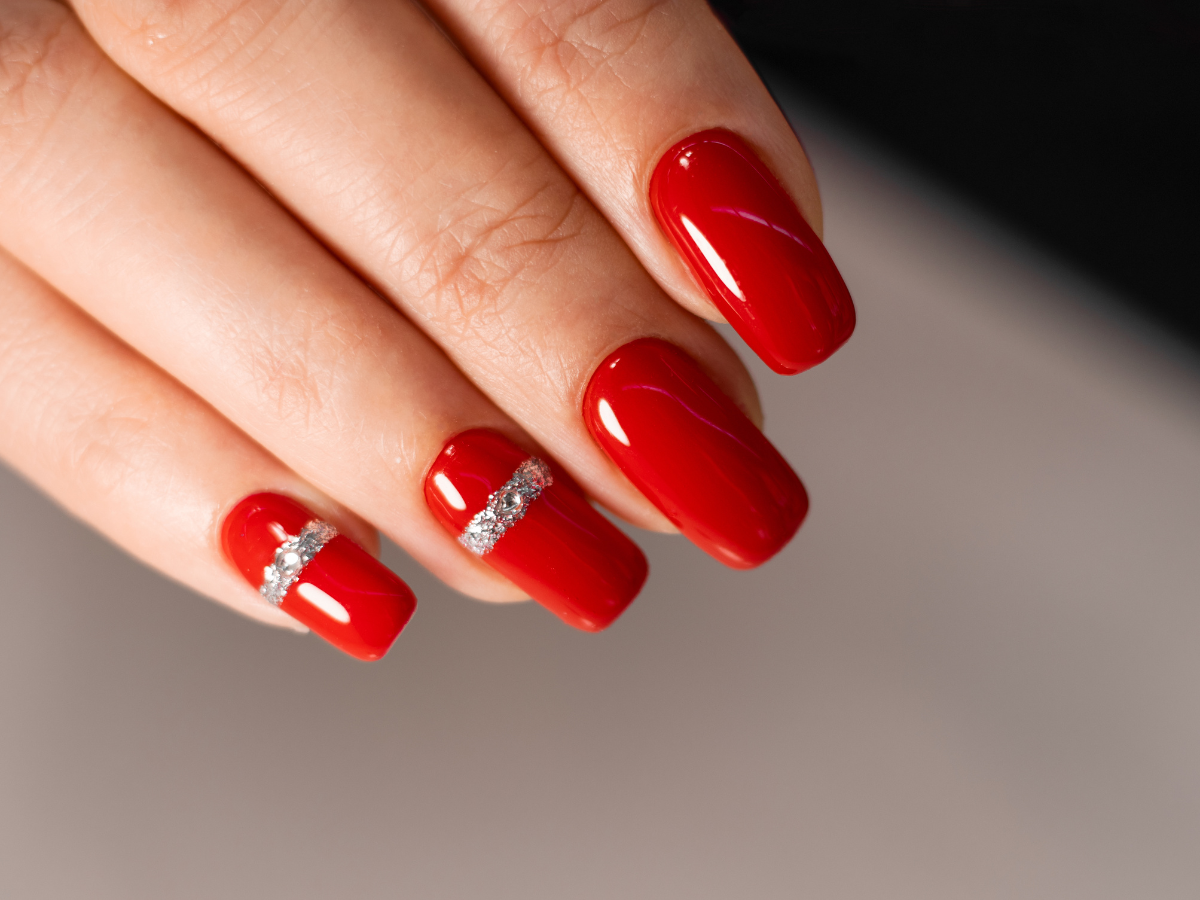 Unhas tendências para inverno 2023. Foto mostra unhas pintadas de vermelho e detalhes em prata