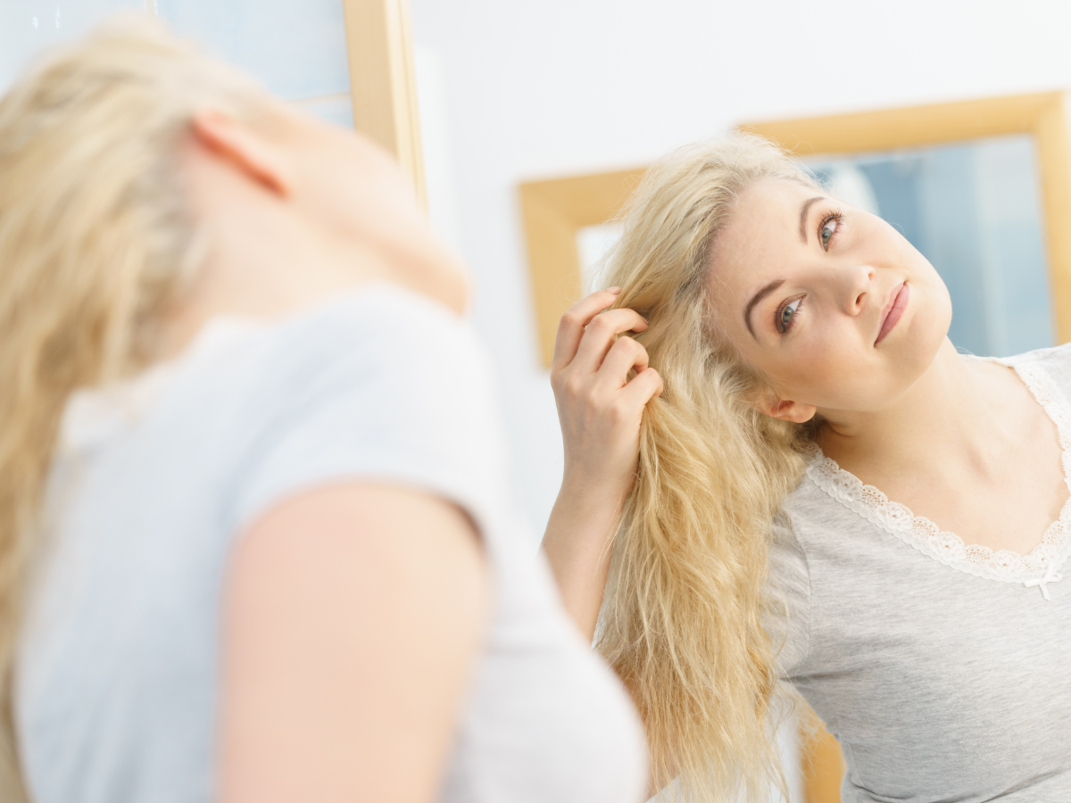Matizar o cabelo em casa. Foto mulher loira olhando no espelhando e passando a mão nos cabelos