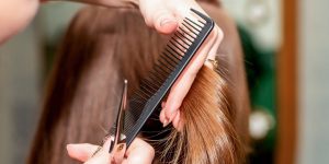 Corte de cabelo ideais para cada tipo de rosto. Foto mostra um cabelo castanho sendo cortado. Pente preto e tesoura prata.