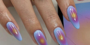 Aura Nails. Foto mostra unhas pintadas de azul claro e com a aura desenhada no centro da unha de rosa e amarelo.