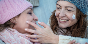Pele e lábios hidratados no inverno. Foto aparece duas mulheres sorrindo passando produtos na pele.