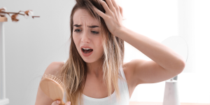 Corte Químico no cabelo. Foto mostra mulher loira olhando para a escova de cabelo assustada