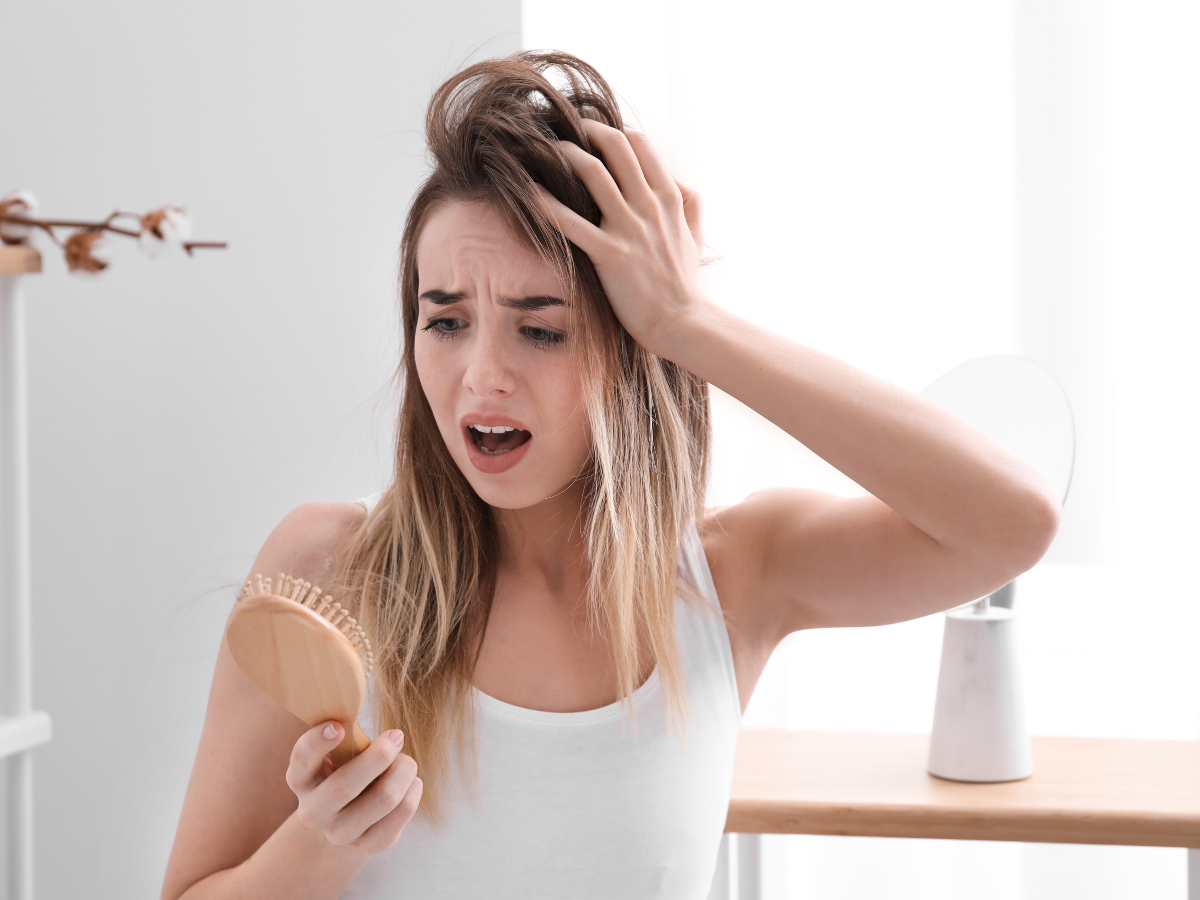 Corte Químico no cabelo. Foto mostra mulher loira olhando para a escova de cabelo assustada