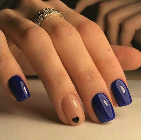 unhas curtas delicadas com cor azul-escuro e um dedo na cor nude com um coração desenhado.