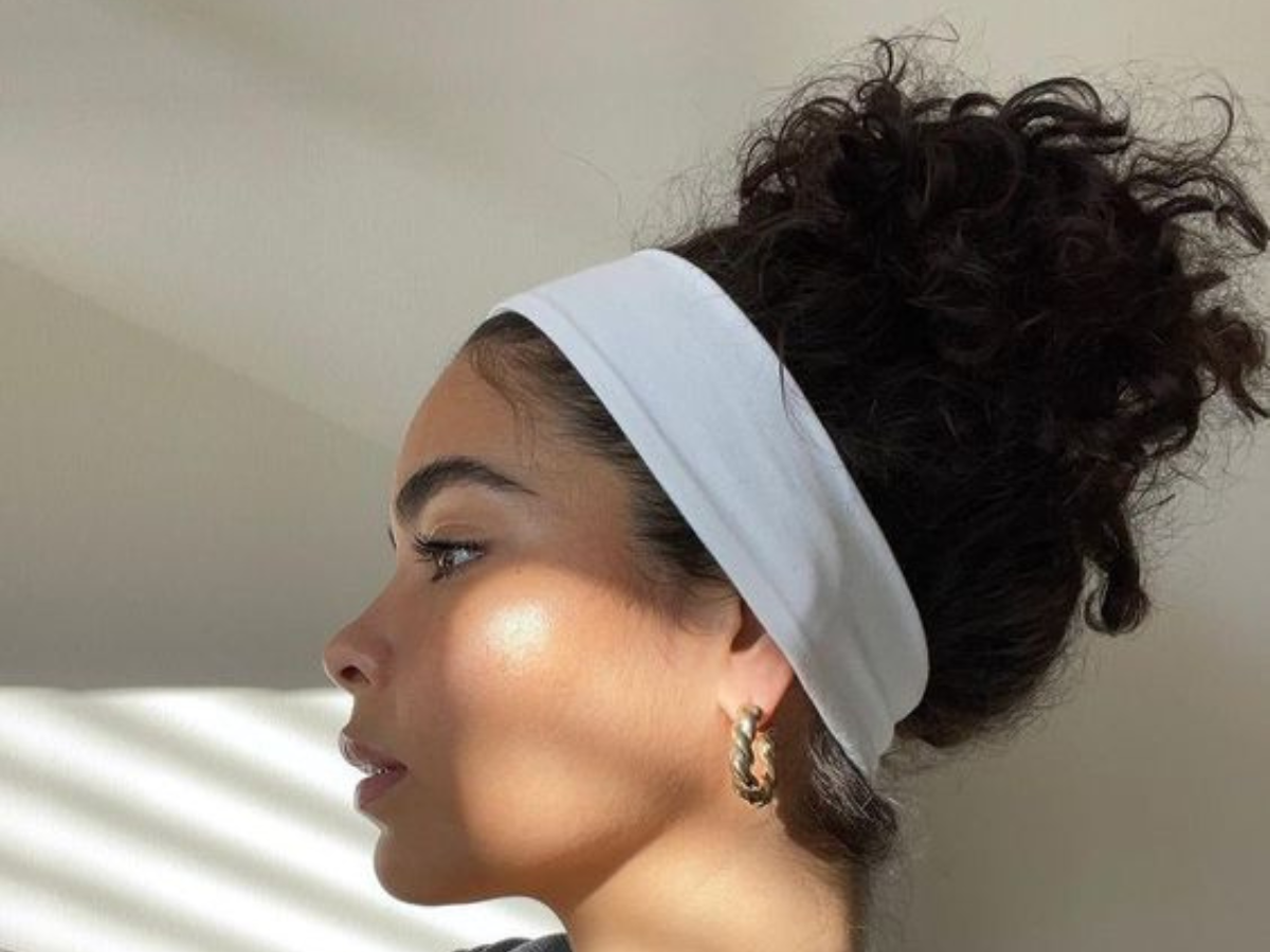 Faixa de Cabelo. Foto mostra mulher negra com faixa no cabelo de cor branca e cabelos com penteado coque.