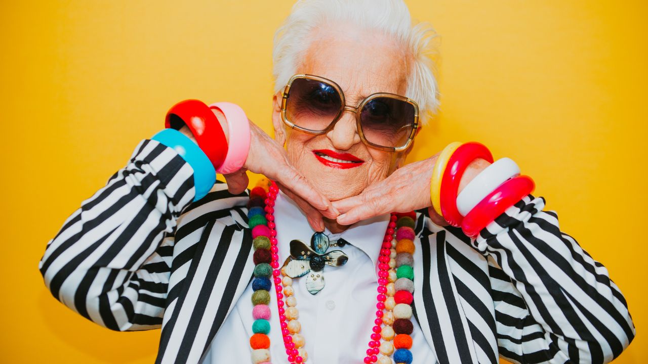 mulher idosa com roupa listrada e várias joias coloridas